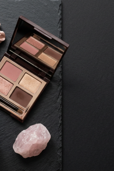 OUAI wave spray and Charlotte Tilbury eyeshadow palette flat lay, Carmella Garcia's beauty bag