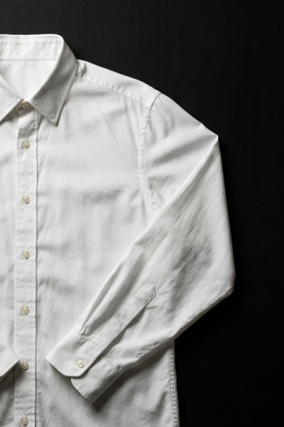Crisp white COS cotton poplin button-down shirt laid flat on matte black background, editorial fashion photography