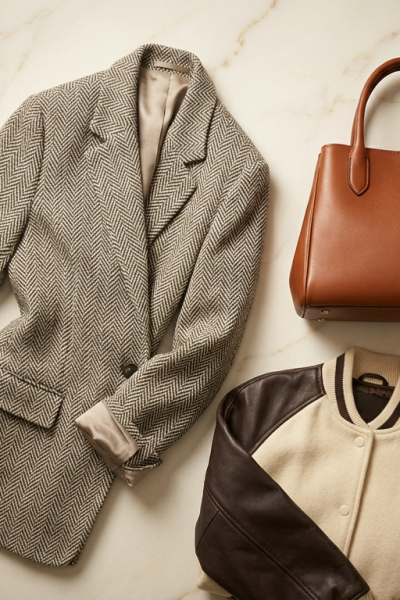 Herringbone tweed blazer, cognac leather bag, and cream varsity jacket with leather sleeves flat-laid on marble, Carole Radziwill fall wardrobe